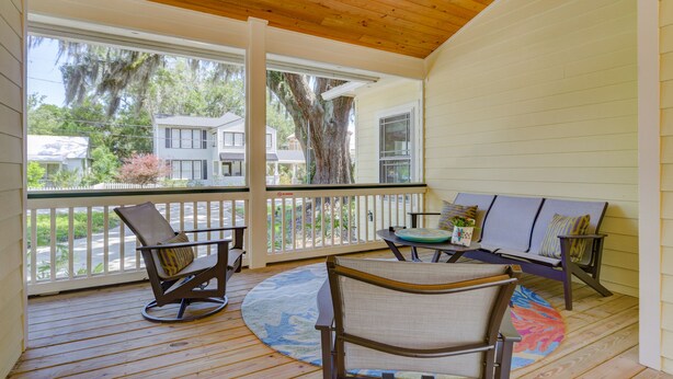 A covered porch with wooden flooring, a rocking chair, a bench, and a table with a rug. - Charming 2BR Uptown Cottage - Artsy & Vibrant! (St. Augustine)