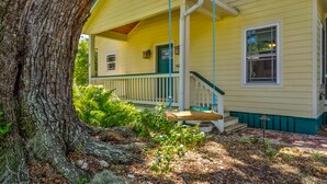A yellow house with a porch, a wooden staircase, and a large tree in the foreground. - Charming 2BR Uptown Cottage - Artsy & Vibrant! (St. Augustine)