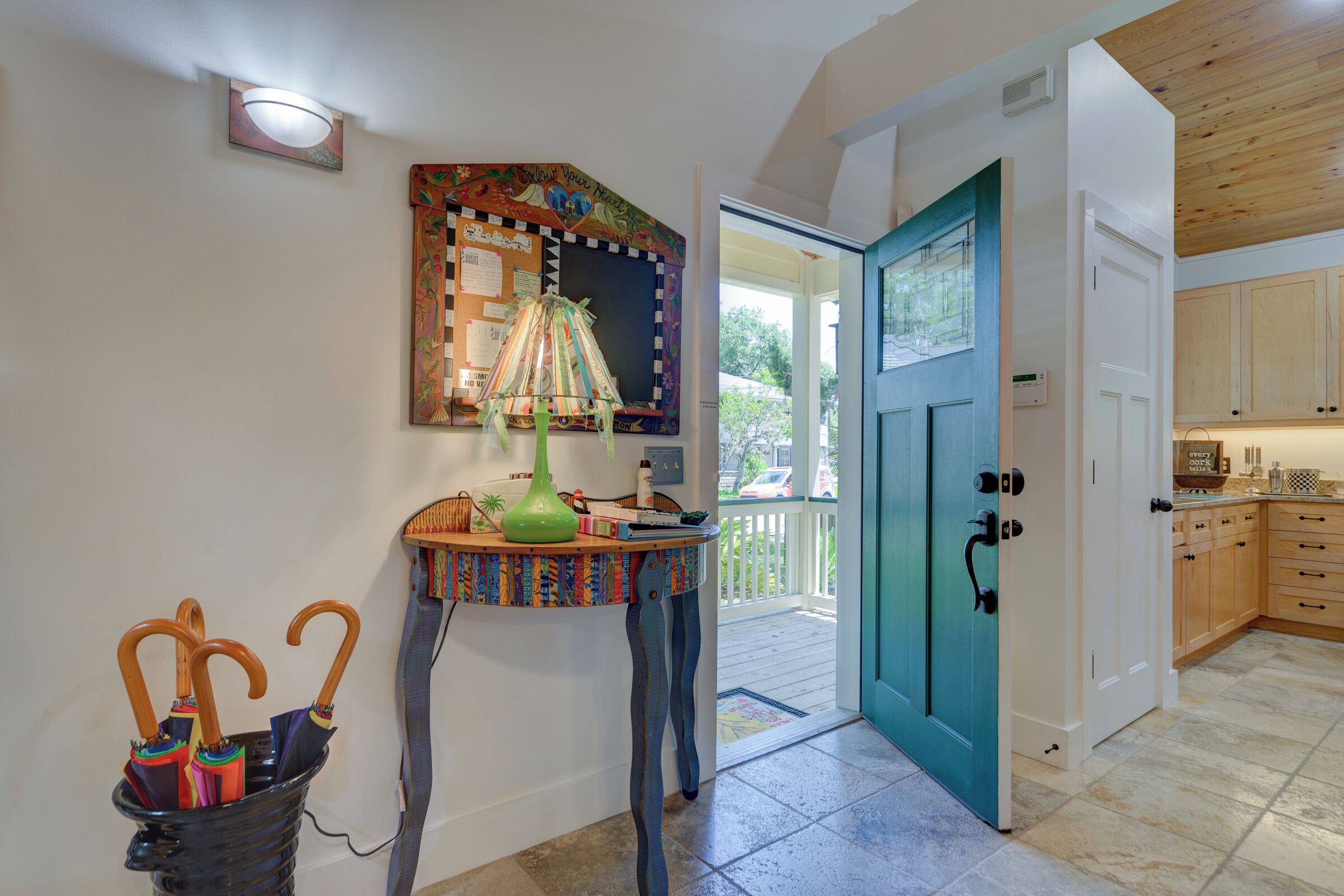 A hallway with a colorful table, a teal door, and a kitchen area.
