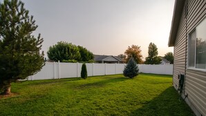 A backyard with a white fence, a small tree, and a house.