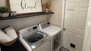 A laundry room with two washing machines, a dryer, a ceiling light, a framed sign on the wall, and a door with a no smoking sign.