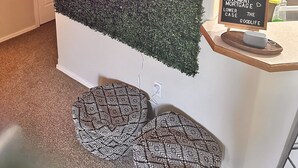 A reception area with a wall covered in foliage and a neon sign that reads "Good vibes only." There is a welcome sign on a stand and a door with a wreath.