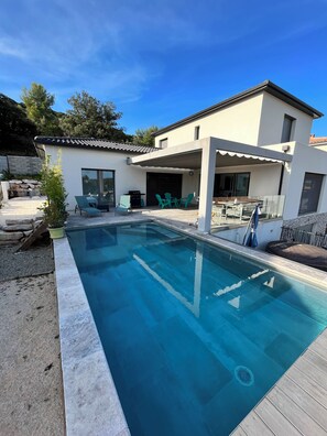 Une maison moderne dotée d’une piscine, d’un espace salon extérieur et d’un patio couvert.