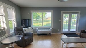 Ein Wohnzimmer mit Fernseher, einer Couch, einem Zweisitzer, einem runden Tisch und einer Bank.
