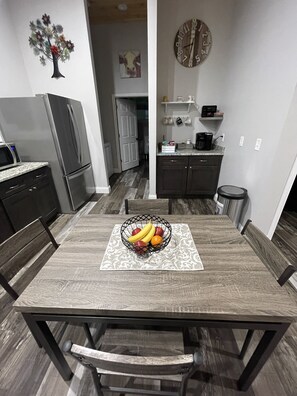 A dining table with a fruit bowl, surrounded by chairs, in a modern kitchen with a refrigerator, microwave, and cabinets. - Mountain view, beautiful and serene! On more than 20 Acres! (Jefferson City)