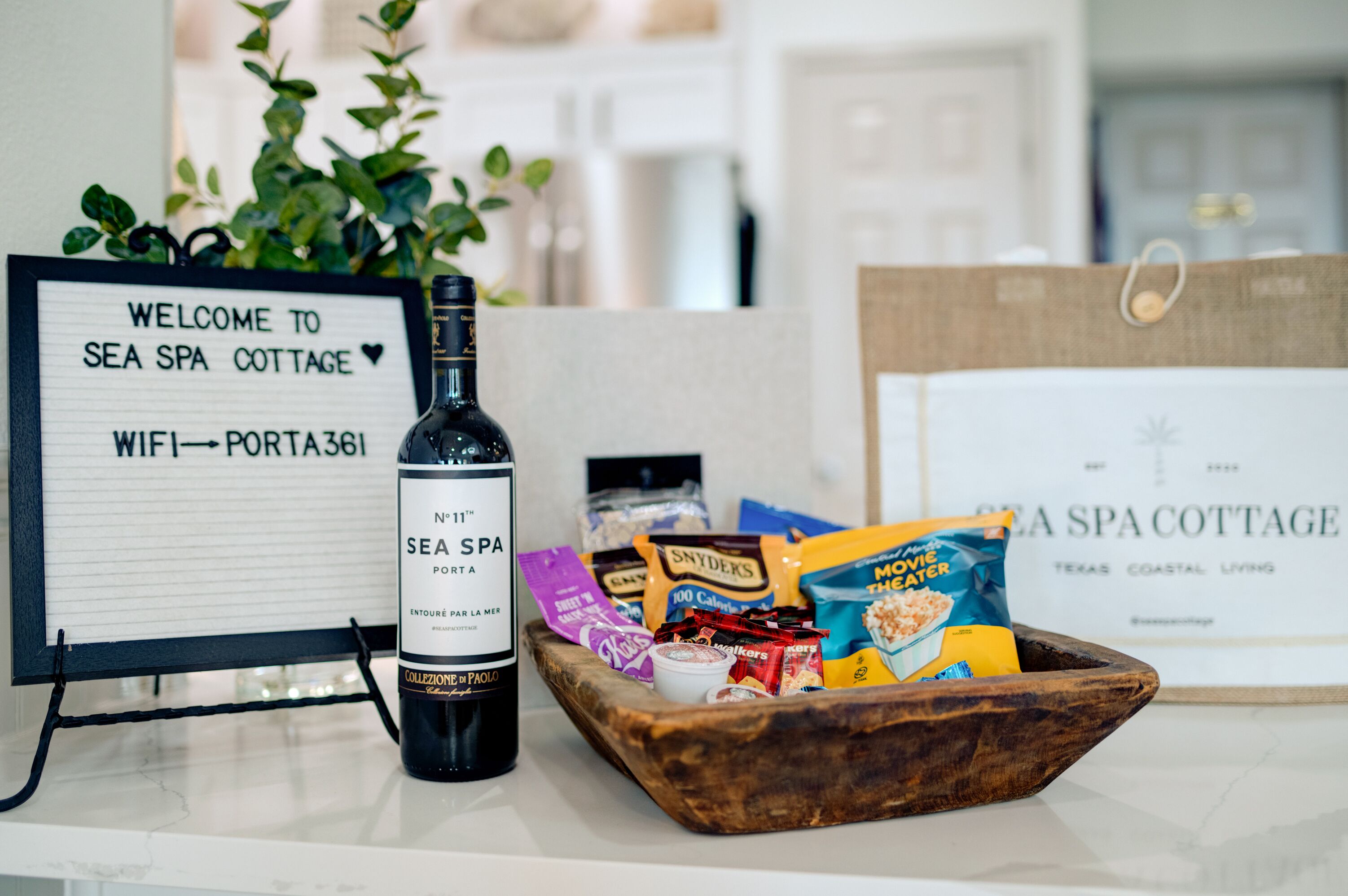 A welcome sign for Sea Spa Cottage, a bottle of wine, and a bowl of snacks.