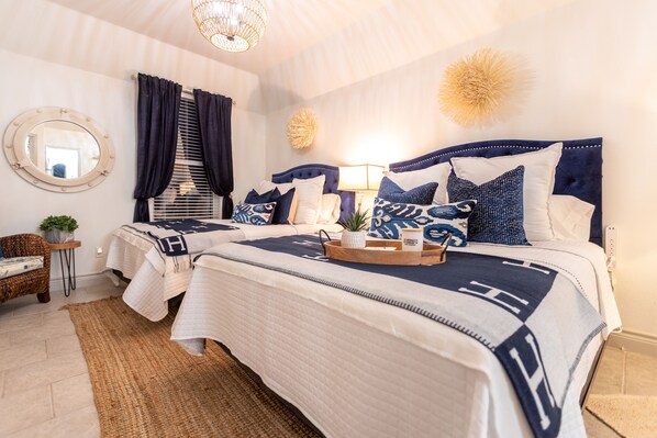 A hotel room with two beds, a round mirror, a potted plant, and a woven rug.