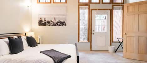 Um quarto com cama, ventilador de teto, janela e porta.