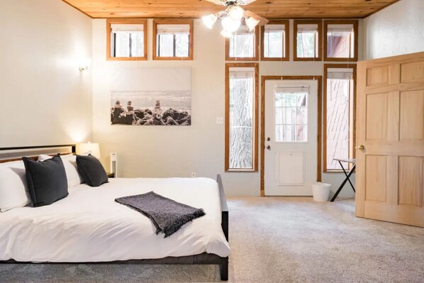 A bedroom with a bed, a ceiling fan, a window, and a door.