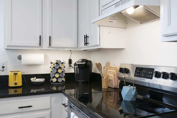 A kitchen with white cabinets, a black stove, a coffee maker, a toaster, and a knife block. - Charming Townhome with Two King Beds & Sep Bath (Cartersville)