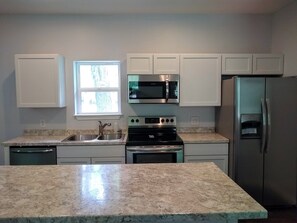 A kitchen with white cabinets, a stainless steel refrigerator, a microwave, an oven, and a dishwasher. - Cottage in the Trees - A getaway from everything, close to everything (Springdale)