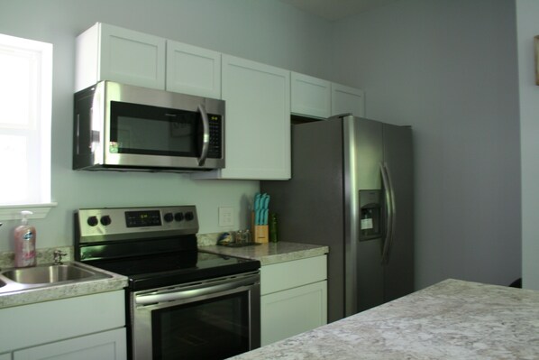 A kitchen with white cabinets, stainless steel appliances including a microwave and refrigerator, a sink, and a countertop. - Cottage in the Trees - A getaway from everything, close to everything (Springdale)