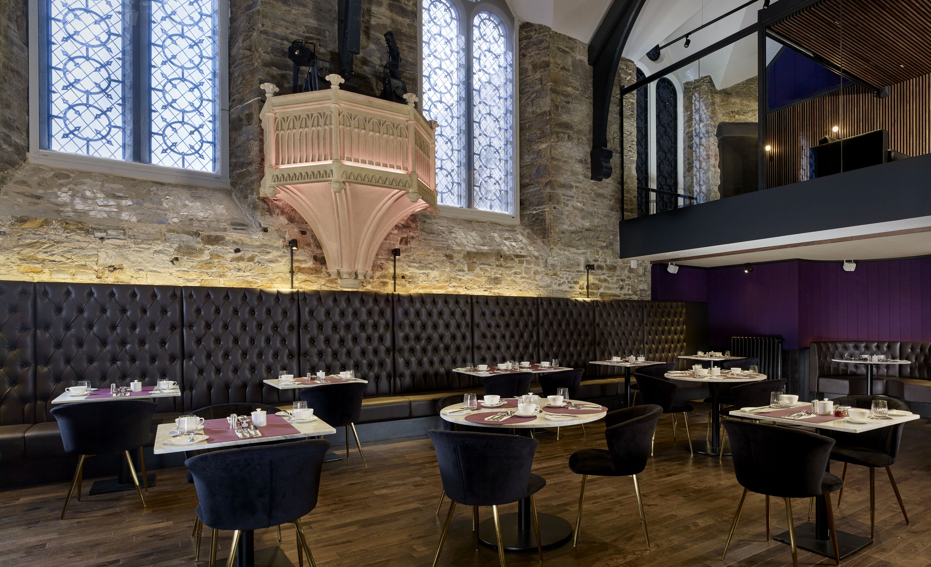 A restaurant with high wooden ceilings, stone walls, and a chandelier. Tables are set with white tablecloths and black chairs.