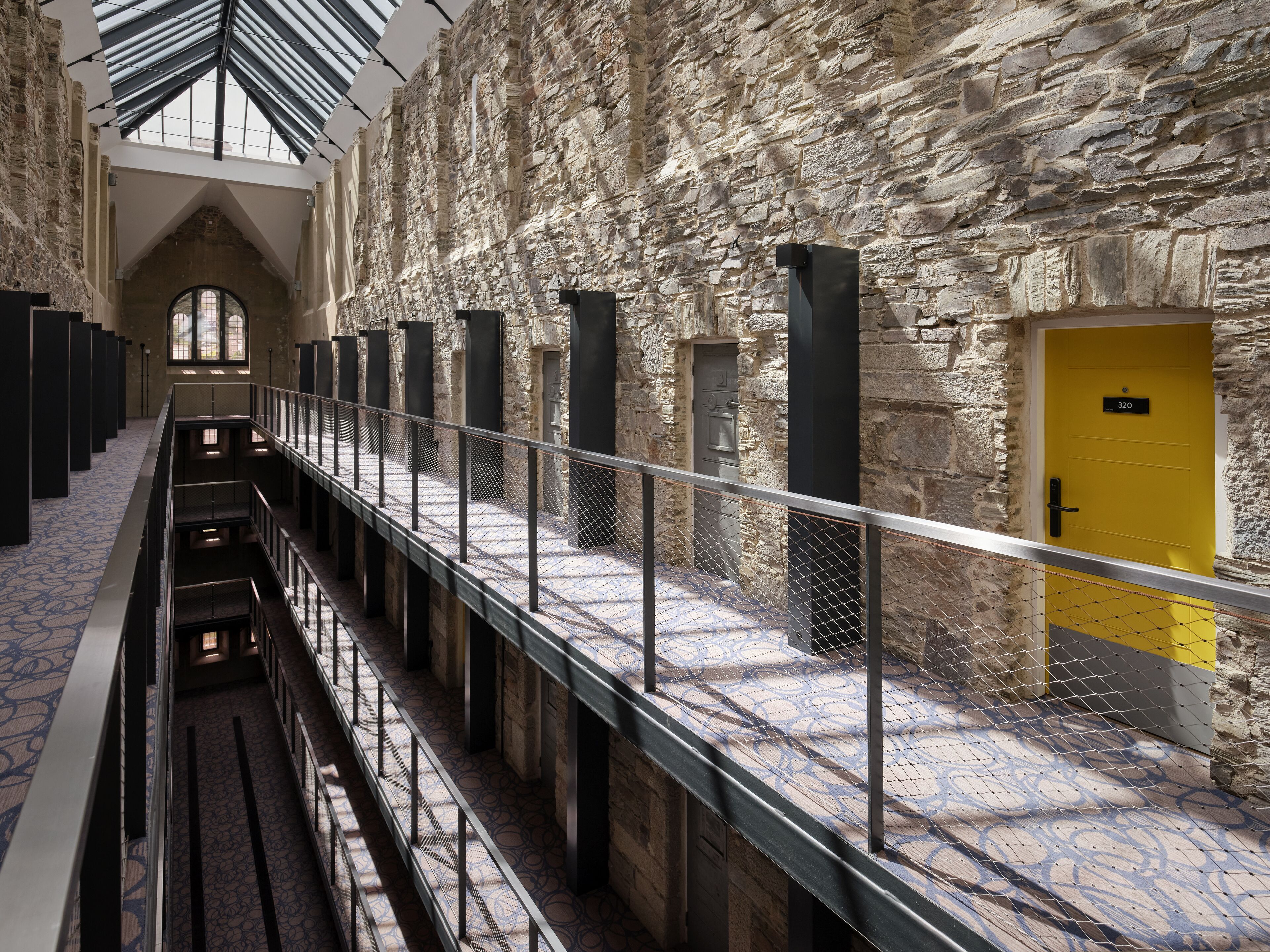 A stone-walled corridor with a yellow door, metal railings, and a patterned floor.