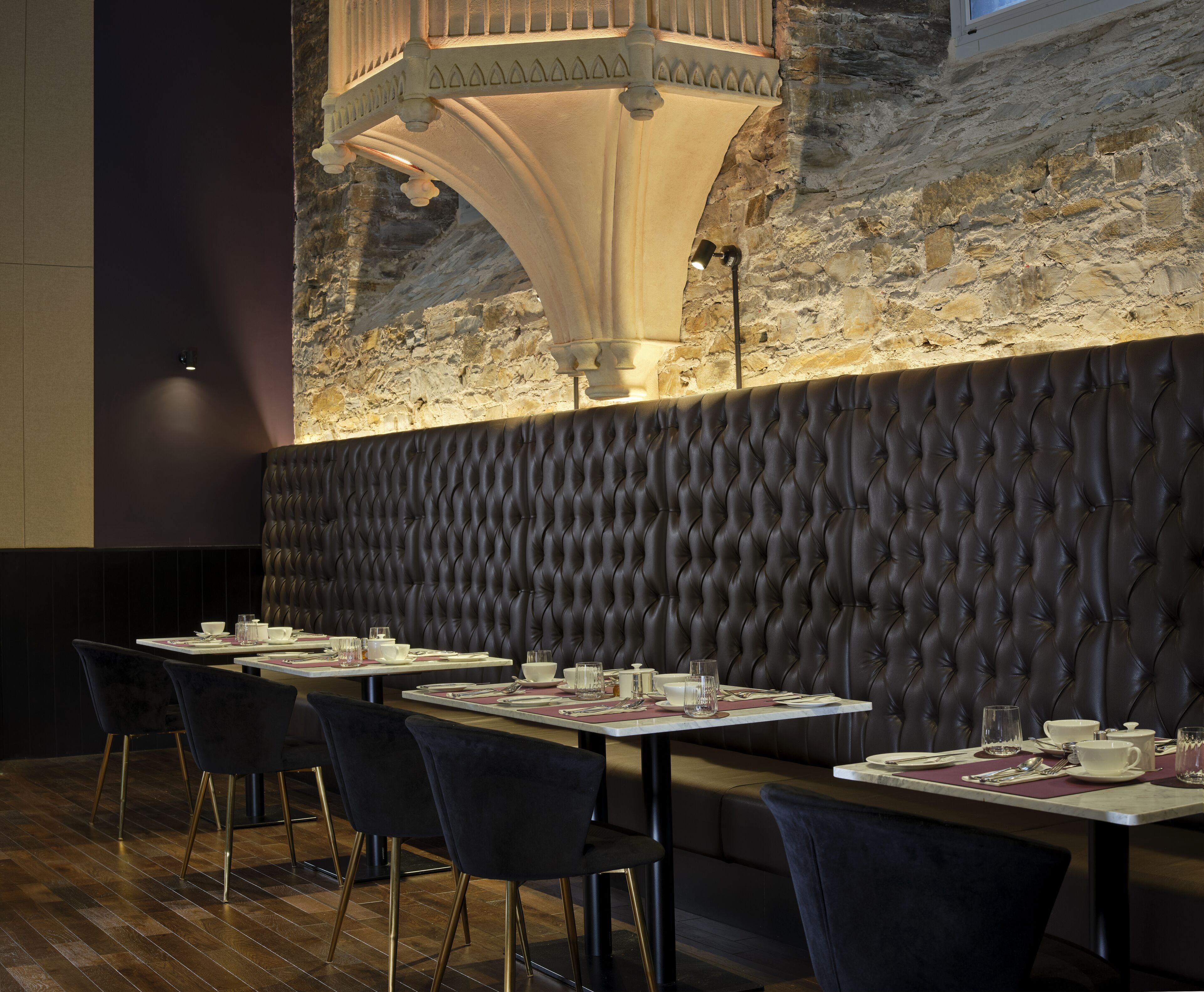 Un restaurant amb un mur de pedra de fons, sòls de fusta i seients tapissats de color negre.