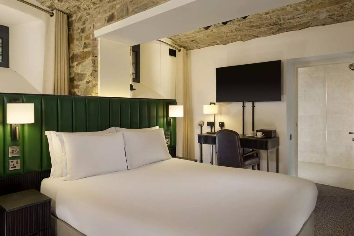 A hotel room with a large bed, two bedside lamps, a desk with a chair, a flat-screen TV, and a stone accent wall.