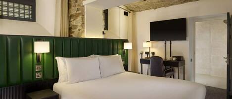 A hotel room with a large bed, two bedside lamps, a desk with a chair, a flat-screen TV, and a stone accent wall.