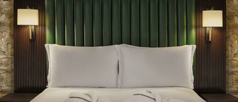 A bed with two pillows and two towels, flanked by two wall-mounted lamps, against a stone wall backdrop.