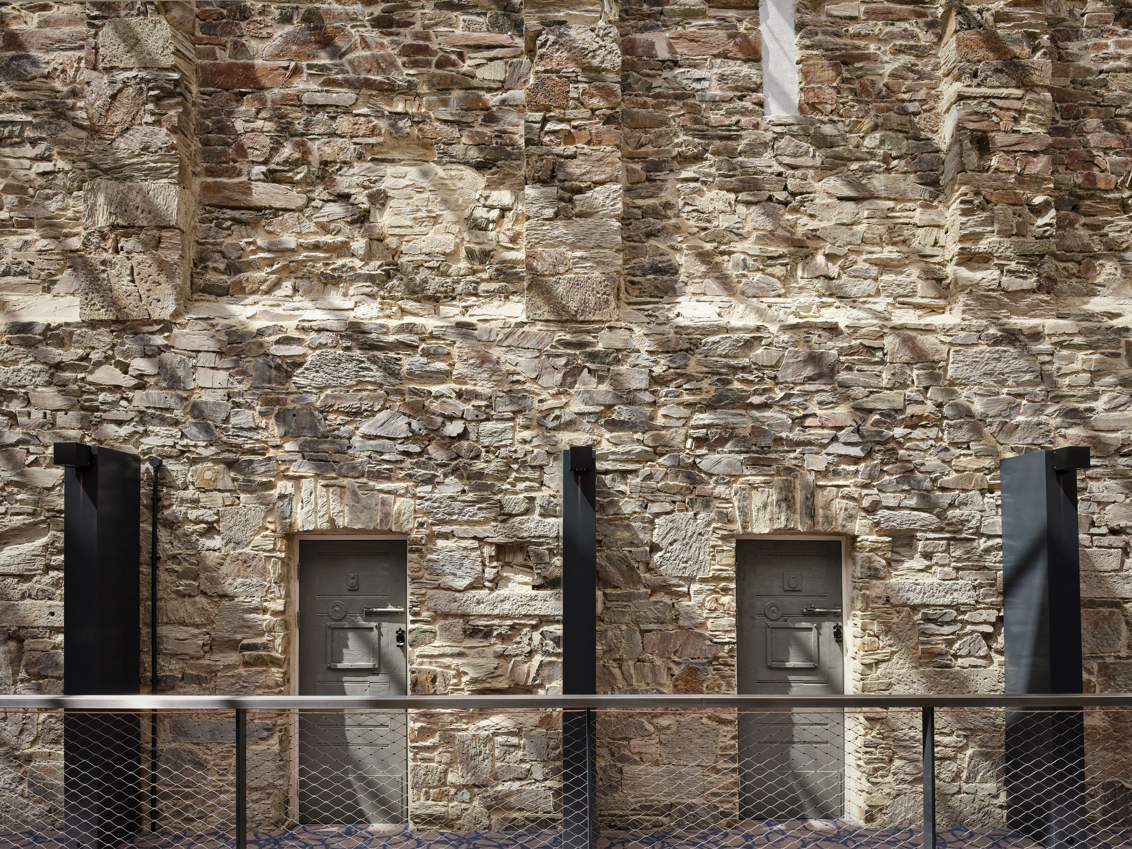Un muro de piedra con tres puertas y una barandilla de metal al frente.