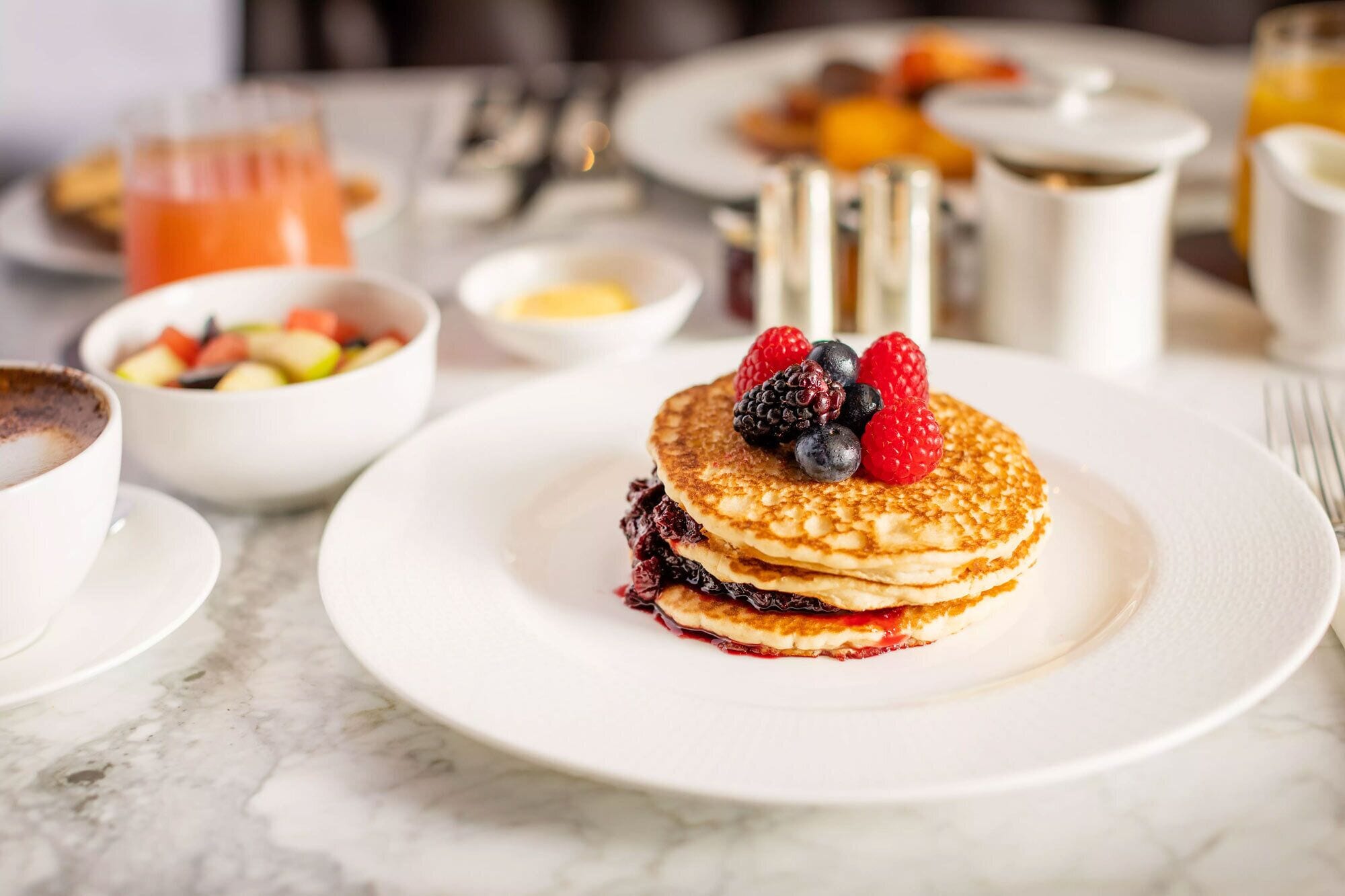 A breakfast setting with pancakes, berries, and a fruit bowl.