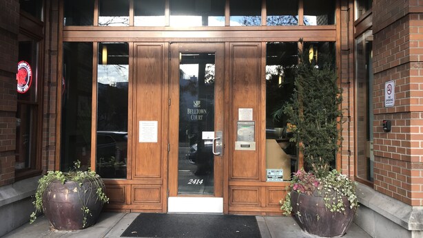 L’entrée d’un bâtiment est marquée par une porte double en bois, un panneau indiquant la présence d’un service de sécurité et un autre panneau interdisant de fumer.