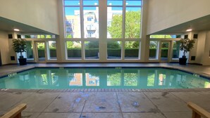 Une piscine intérieure à l’eau d’un bleu limpide, dotée de grandes fenêtres et agrémentée de plantes en pot.