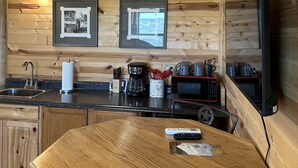 A wooden cabin interior with a mounted deer head, framed pictures, a kitchen area with a sink, stove, and microwave, and a dining table. - Arrowhead Cabin at Wolf Creek Guest Ranch (Fredericksburg)