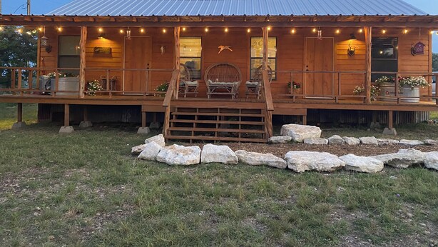 A wooden cabin with a porch, stone seating, and string lights. - Arrowhead Cabin at Wolf Creek Guest Ranch (Fredericksburg)