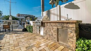 Un patio al aire libre con piso de piedra, chimenea de piedra, una parrilla y un banco.