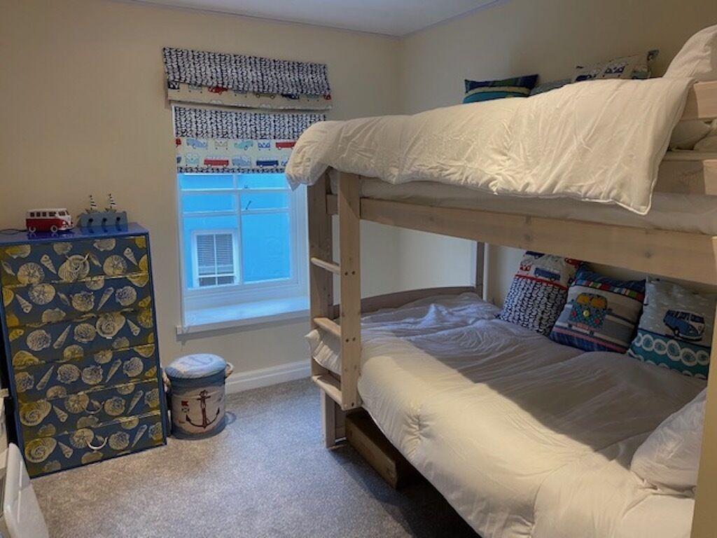 A bunk bed room with a window, a dresser, and a toy car on the dresser.