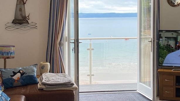 A room with a view of a calm sea, a bed with pillows, a lamp, and a small table.