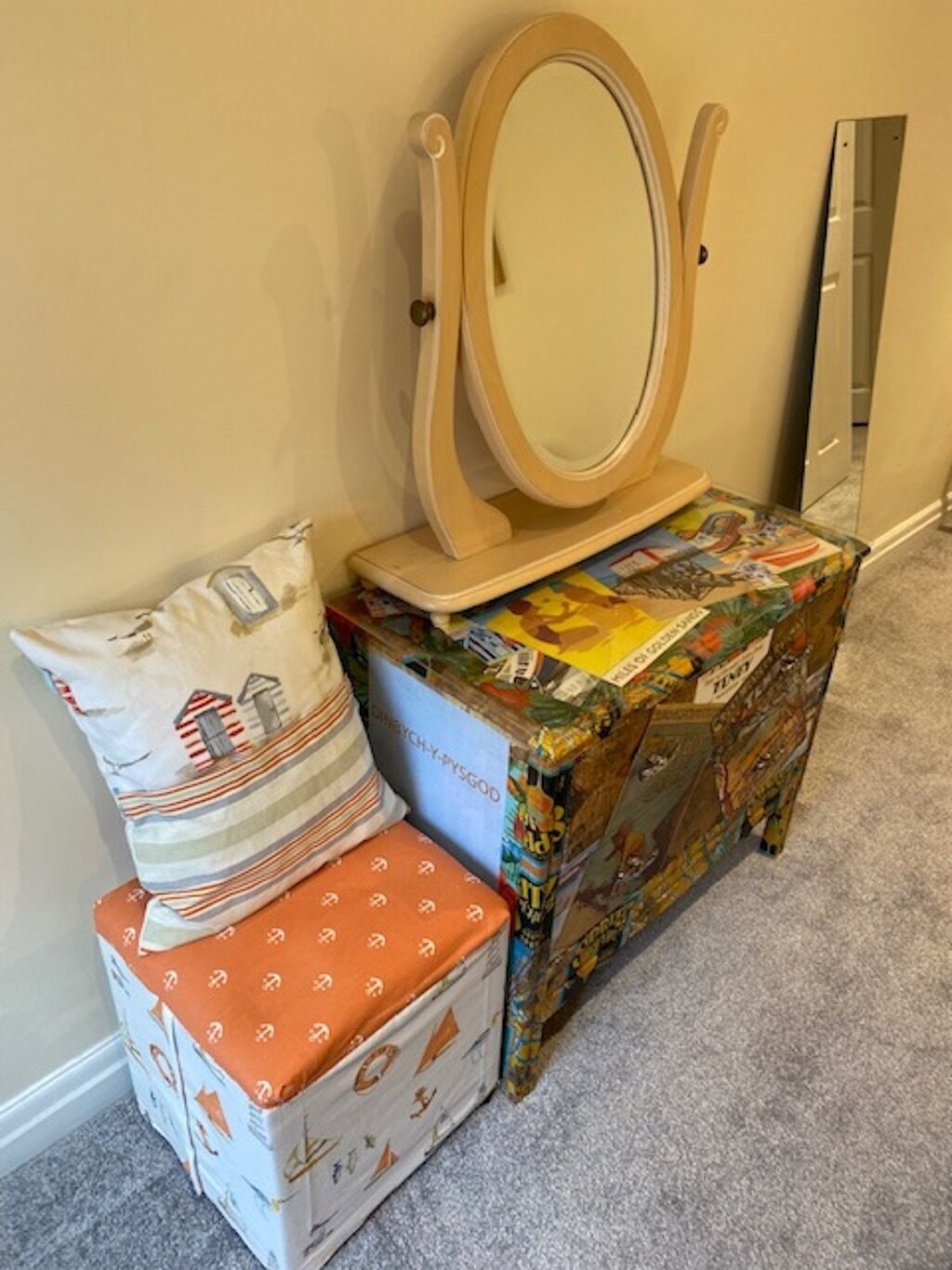 A corner with a wooden vanity, a mirror, a patterned pillow, and a small box with a colorful cover.