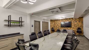 A conference room with a marble table, black chairs, a mounted TV, and a wall-mounted shelf with plants.