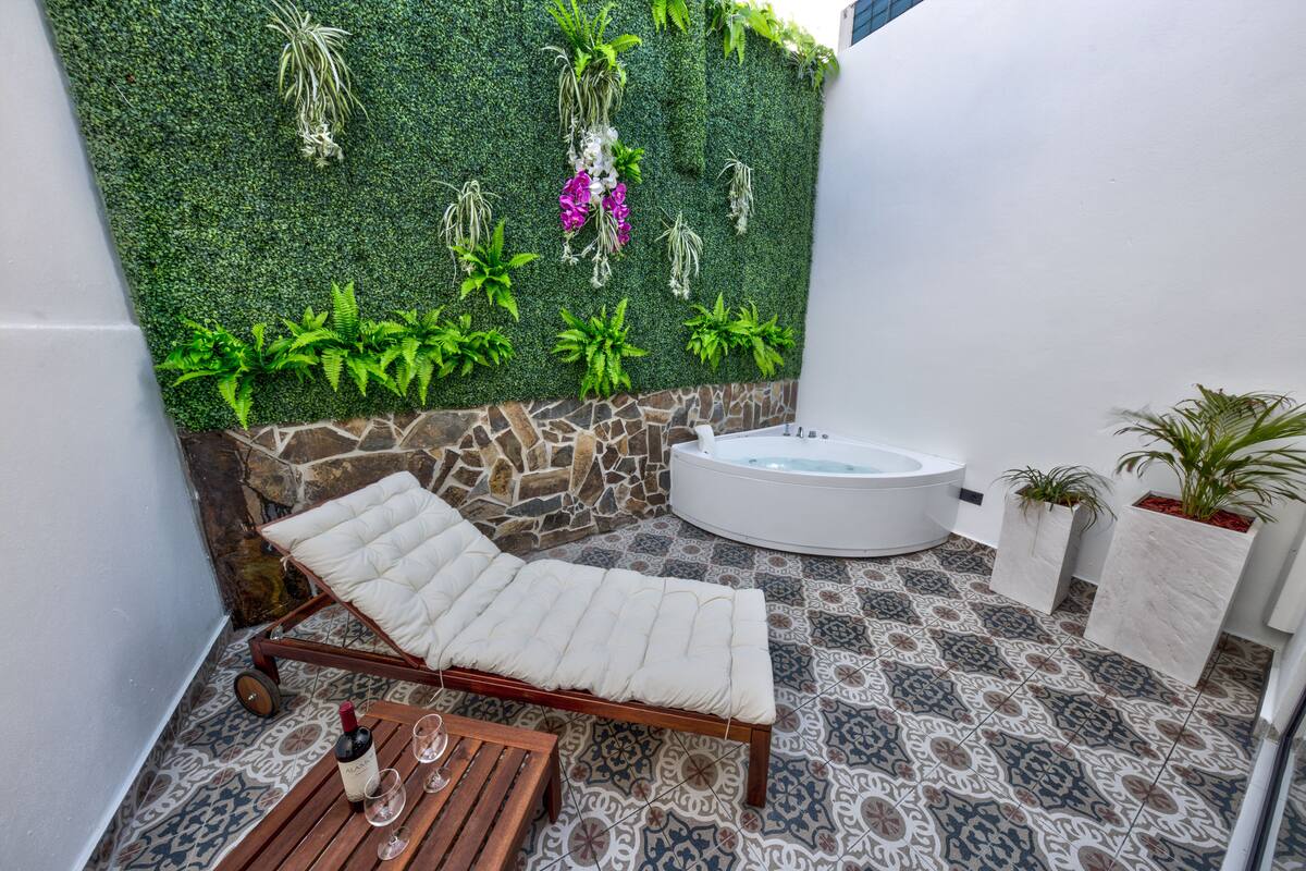 A spa area with a lounge chair, a hot tub, and a wall adorned with plants.