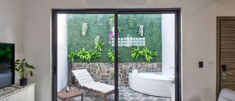 A modern living room with a large sliding glass door leading to a patio area with a stone wall and greenery.