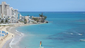 A beach with a sailboat, a pier, and buildings in the background. - Hotel Puerto Valdes (San Juan)
