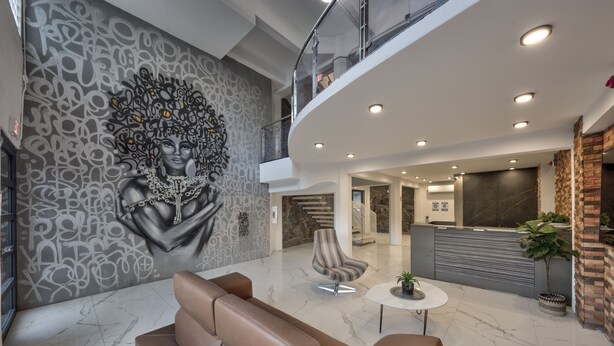 A modern lobby with a marble floor, a reception desk, a seating area with leather sofas, and a decorative wall mural. - Hotel Puerto Valdes (San Juan)