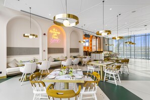 Ein modernes Restaurant mit weißer und goldener Einrichtung, mehreren Essbereichen und einer Neonreklame.