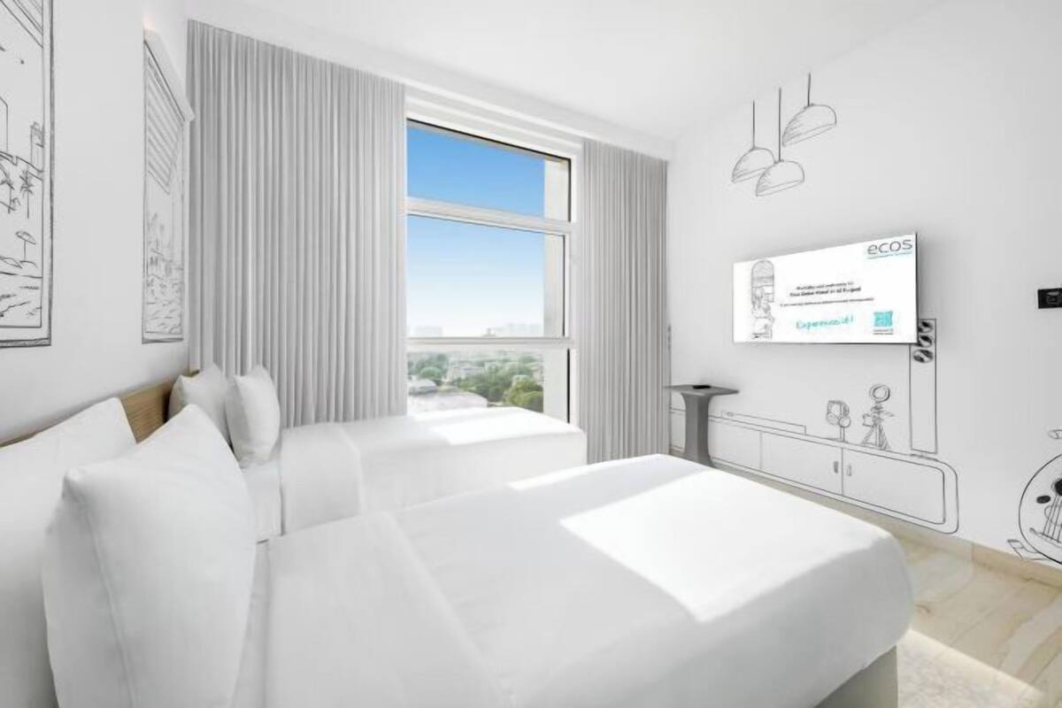Ein Hotelzimmer mit zwei Betten, einem großen Fenster, einem Wand-Fernseher und Blick auf die Stadt.