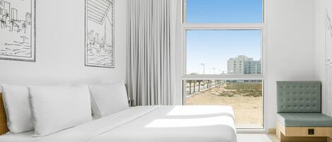 A modern bedroom with a large bed, a view of the beach, and a balcony.