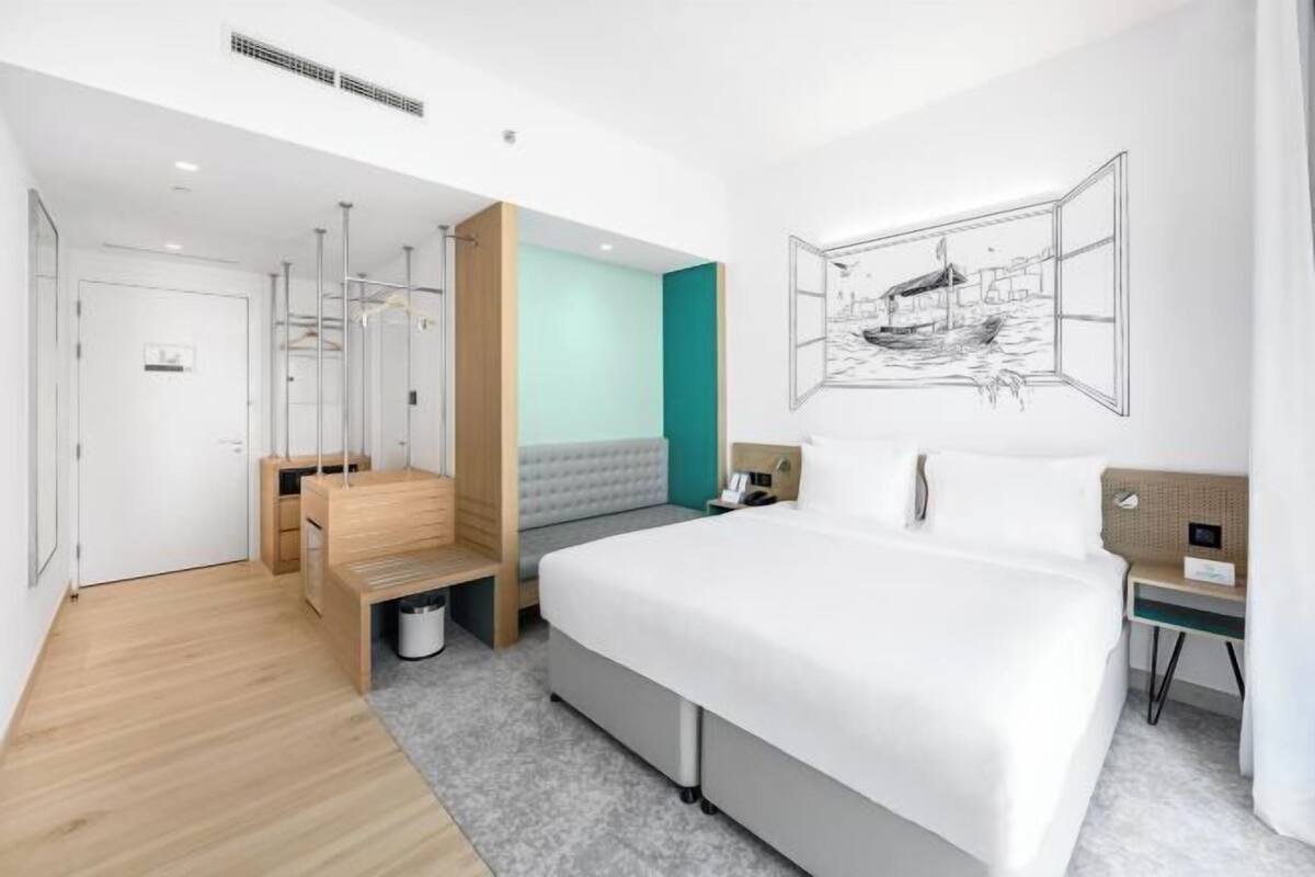 Ein modernes Hotelzimmer mit einem großen Bett, einem Schreibtisch, einem Stuhl, einem Kleiderschrank und einem Badezimmer.