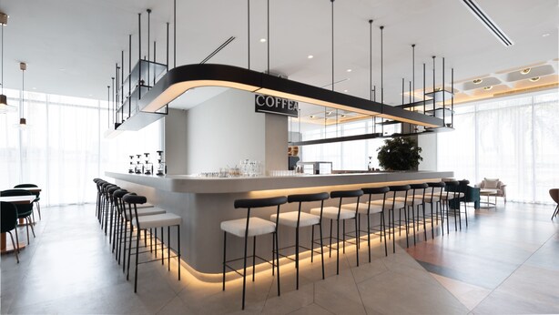 Een moderne bar met een 'COFFEE' bord, barkrukken en een keuken op de achtergrond.