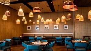 Un restaurant aux murs en bois, aux chaises bleues et aux lampes en osier suspendues au plafond.
