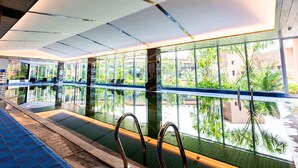 Une piscine intérieure avec des parois en verre transparent, un sol bleu à texture et des rampes métalliques.