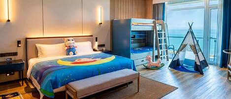 A modern hotel room with a large bed, a desk, a wardrobe, a tent, and a view of the sea.