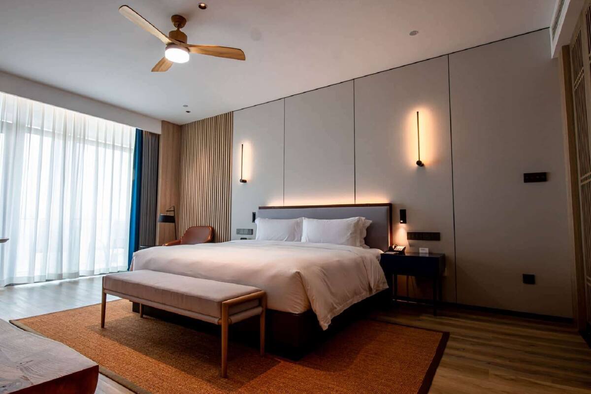 Ein modernes Hotelzimmer mit einem großen Bett, einem Schreibtisch, einem Stuhl und einem Deckenventilator.