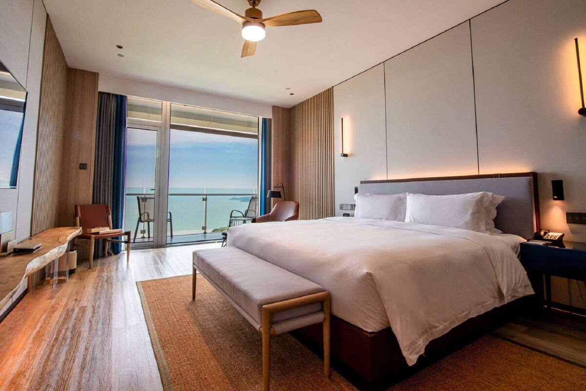 Ein modernes Hotelzimmer mit einem großen Bett, einem Schreibtisch, einem Stuhl und einem Balkon mit Meerblick.