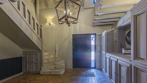 A hallway with a staircase, a chandelier, and a door leading outside.