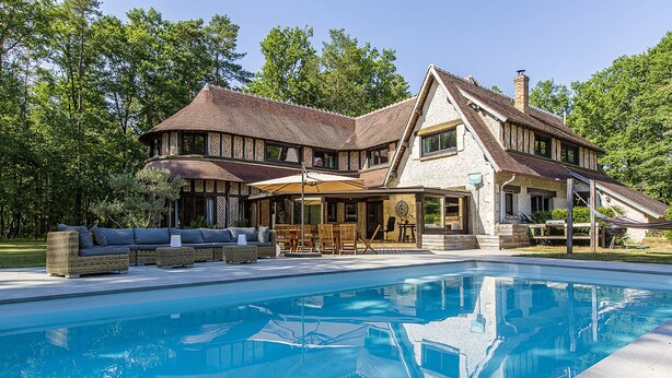 A large house with a swimming pool, outdoor seating, and a covered patio area.