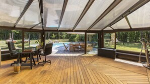 A covered outdoor area with a wooden deck, seating, and a view of a swimming pool.